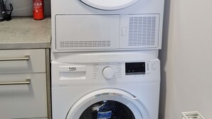Een wasmachine met voorlader, een bedieningspaneel en een fles wasmiddel op het aanrecht.