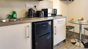Een moderne keuken met een ingebouwde vaatwasser, een koffiezetapparaat en een magnetron. Er staat een glazen tafel met twee stoelen en een schaal met fruit.