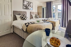 Een hotelkamer met twee bedden, een glazen bijzettafeltje met een schaal gebakjes, en uitzicht op het exterieur door grote ramen.