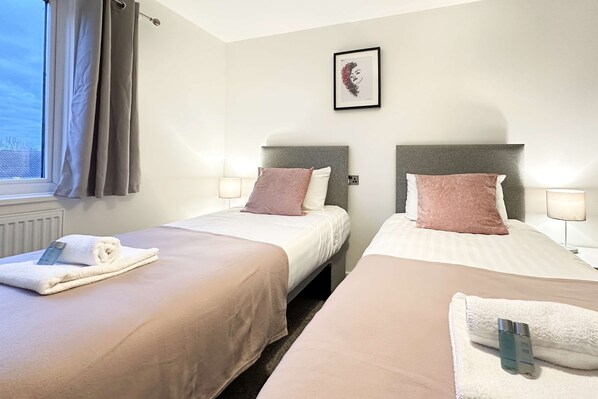 Habitación de hotel con dos camas, ropa de cama color beige, una obra de arte enmarcada en la pared y una ventana con cortinas.