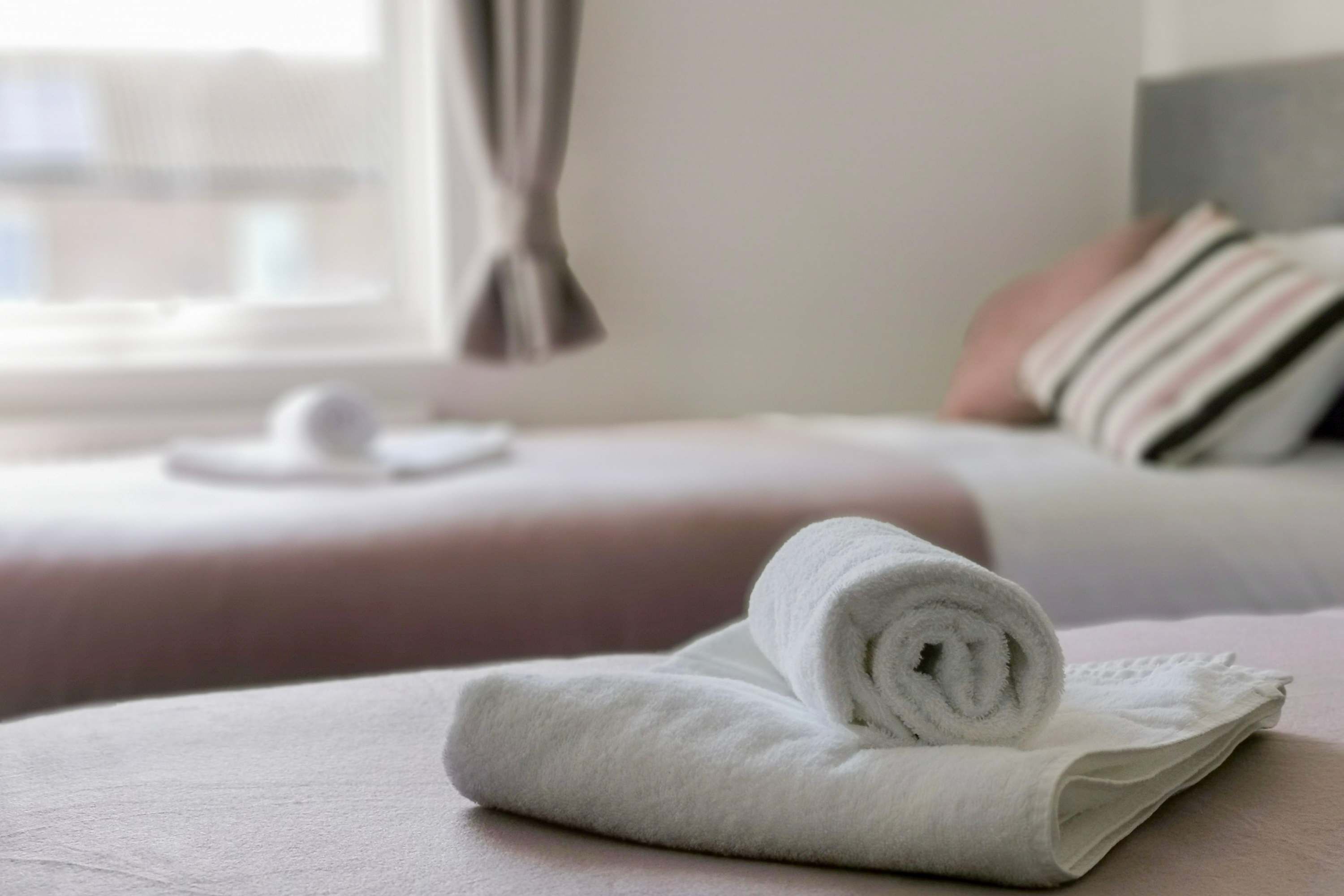A neatly made bed with a rolled white towel on the bed.