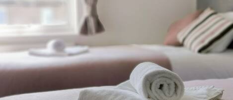 A neatly made bed with a rolled white towel on the bed.