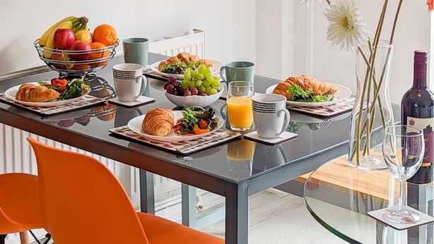 A breakfast table with croissants, fruit, and juice, and a bottle of wine on a glass table.