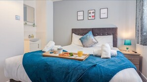 A neatly made bed with a blue blanket, a tray with food and drink, and a bedside table with a lamp.