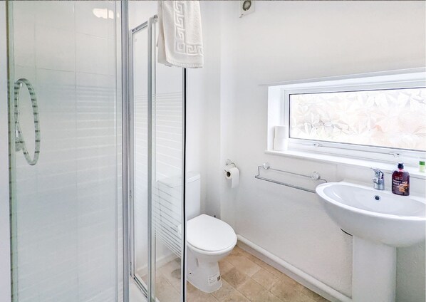 A bathroom with a glass shower enclosure, a toilet, a sink with a window above it, and a towel rack.