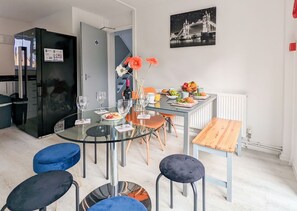 Eine moderne Küche mit einem schwarzen Kühlschrank, einem Glastisch mit Stühlen und einer Frühstücksvorrichtung mit Obst und Gebäck.