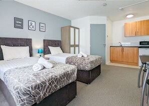 Ein Hotelzimmer mit zwei Betten, einer kleinen Küchenzeile und einem Badezimmer mit Spiegel.