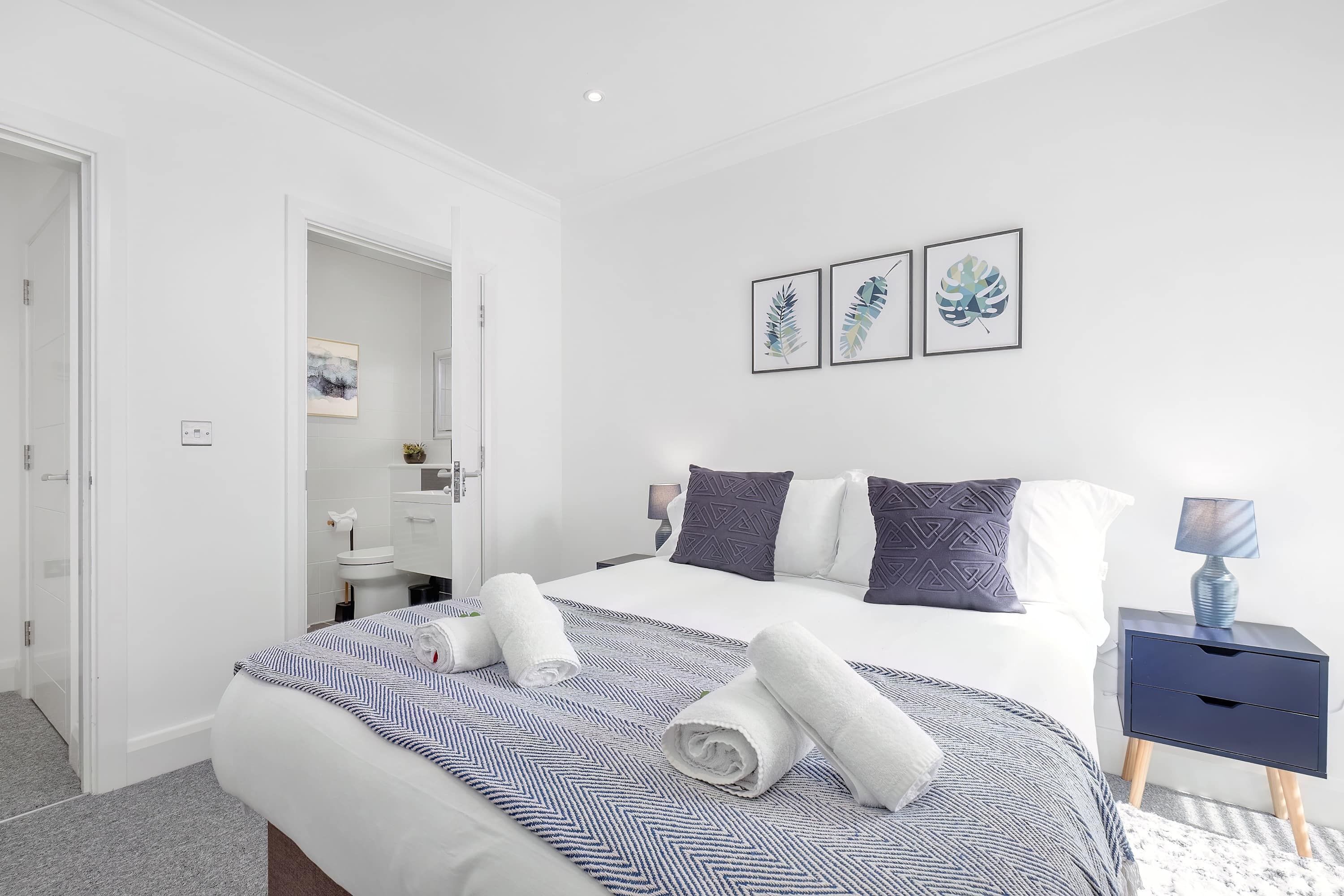 A modern hotel room with a neatly made bed, a bedside table with a lamp, and a bathroom visible through an open door.