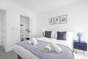 Een moderne hotelkamer met een net opgemaakt bed, een nachtkastje met een lamp, en een badkamer zichtbaar door een open deur.