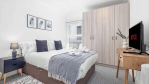 Un dormitorio moderno con cama, mesita de noche, televisor, armario y una obra de arte en la pared.