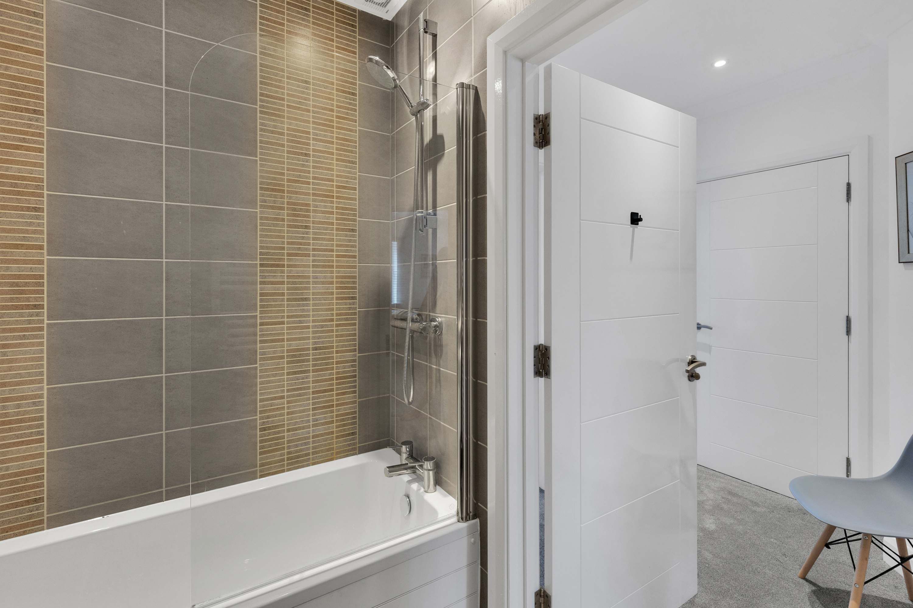 Een moderne badkamer met een douchecabine van glas, een witte badkuip en een grijze stoel.