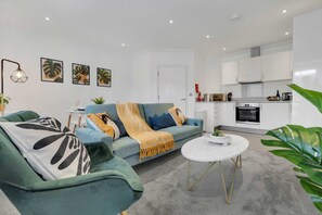Een moderne woonkamer met een blauwgroene bank, een ronde salontafel en een keuken op de achtergrond.