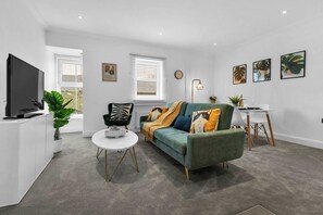 Een moderne woonkamer met een bank, een salontafel, een televisie en een eethoek met een kleine tafel en stoelen.