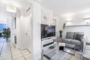 A modern living room with a flat-screen TV, a grey sofa, and a glass coffee table. - Elegant 4BR House Near City Centre Angus Suites (Peterborough)
