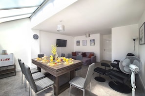 Ein modernes Wohnzimmer mit Essbereich, einem Flachbildfernseher und Deckenventilator.