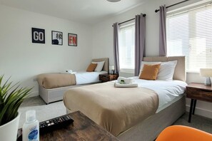 A hotel room with two beds, a small table with a remote control, a potted plant, and a window with curtains. - Last Minute Deals 4BR House of Four Chimneys (Peterborough)