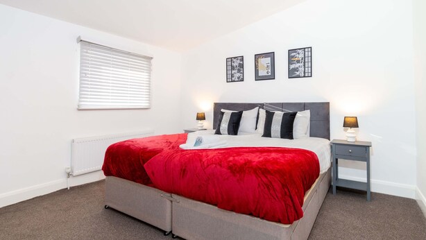 A bedroom with a bed, a radiator, a window with blinds, and two bedside tables with lamps.