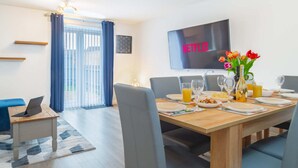 A dining area with a wooden table set for four, a laptop on a side table, and a TV mounted on the wall displaying "NETFLIX".