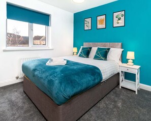 A modern bedroom with a large bed, teal walls, and a window with a view of a building.