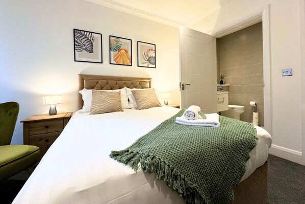 A neatly made bed with a green blanket, a headboard, and three framed artworks on the wall.