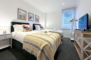 A hotel room with a large bed, a desk with a computer, a TV, and framed pictures on the wall.