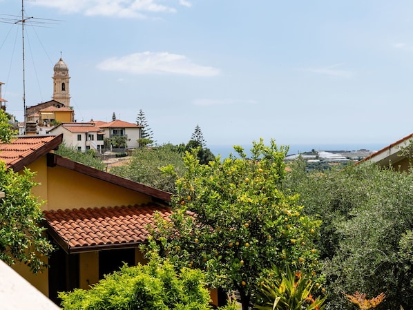 A residential area with a prominent church tower, lush greenery, and a view of the sea.