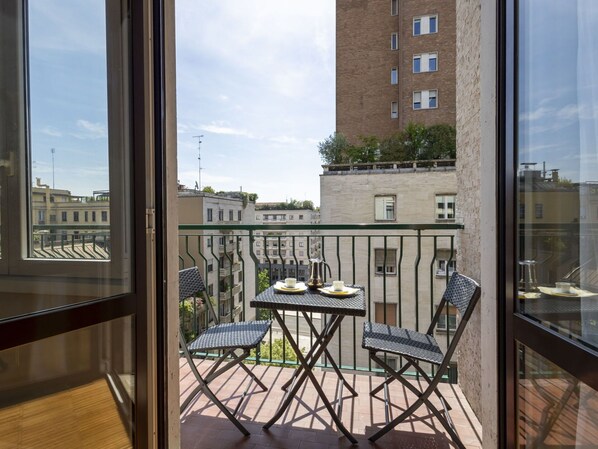 A balcony with a table and chairs, a view of buildings, and a clear sky.