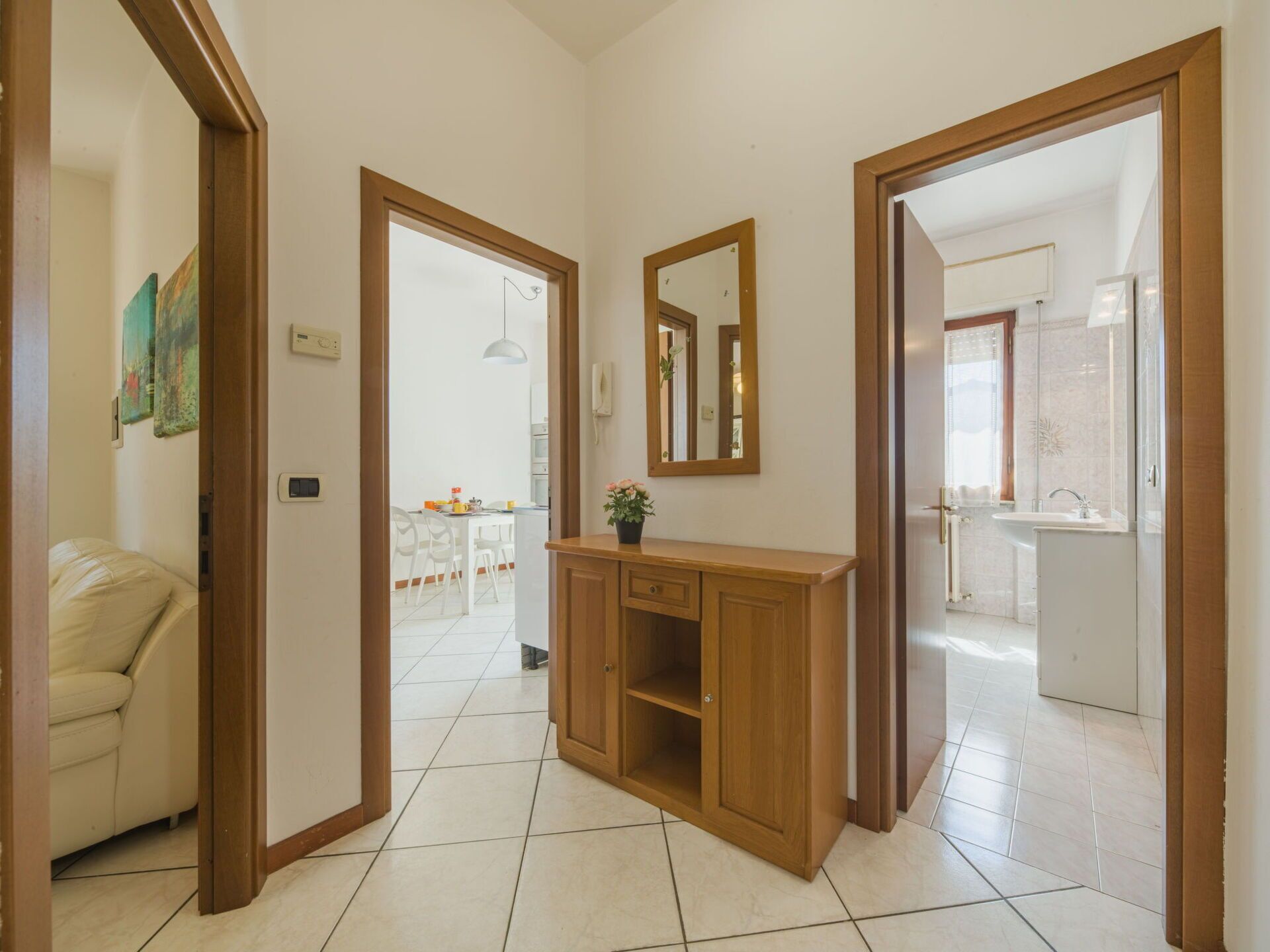 A hallway with a wooden cabinet, a mirror, and a door leading to a bathroom.