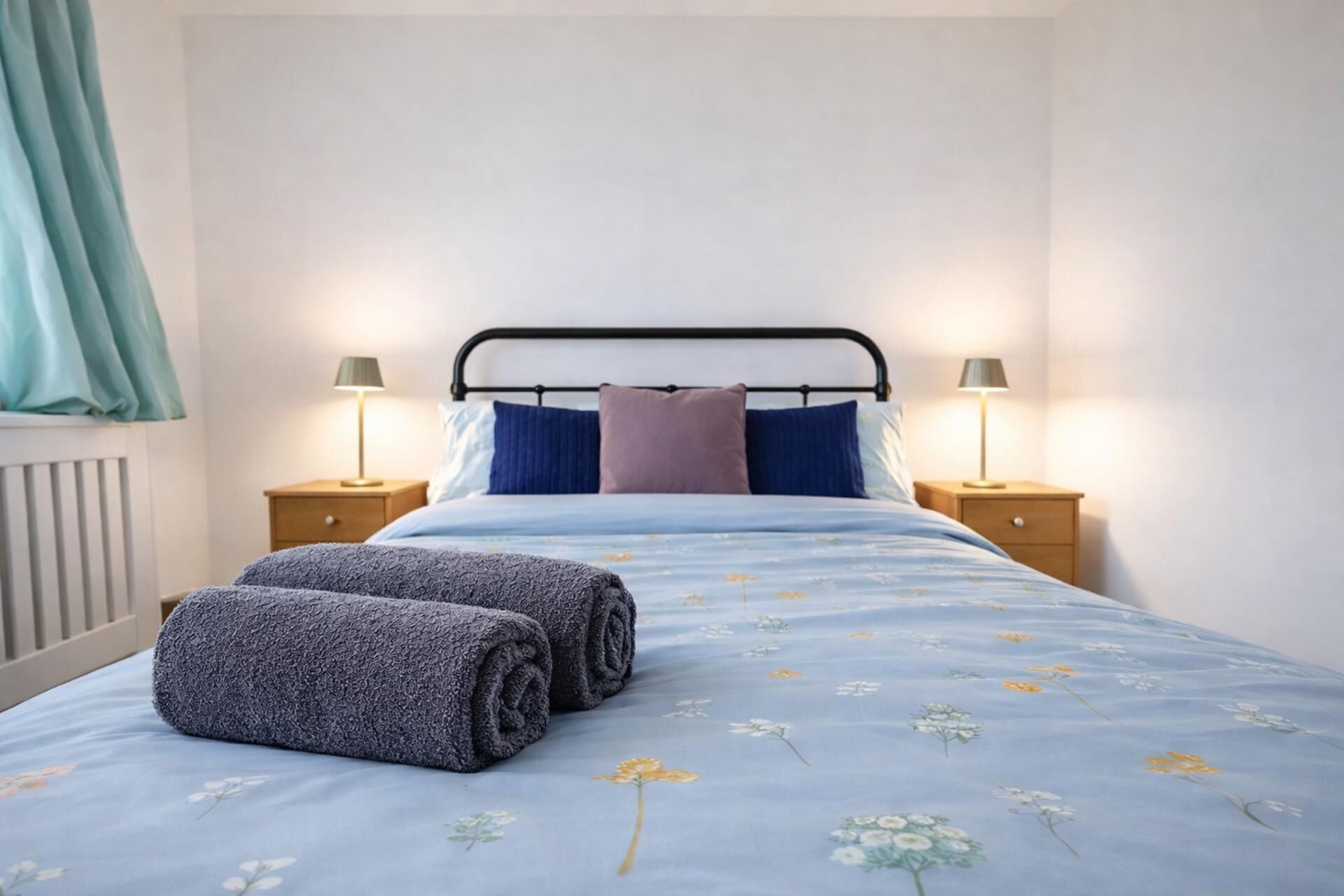 A bedroom with a bed, two bedside tables, a nightstand, a window with curtains, and a radiator.