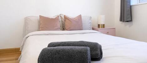 A neatly made bed with pillows, a bedside table with a lamp, and a window with curtains.