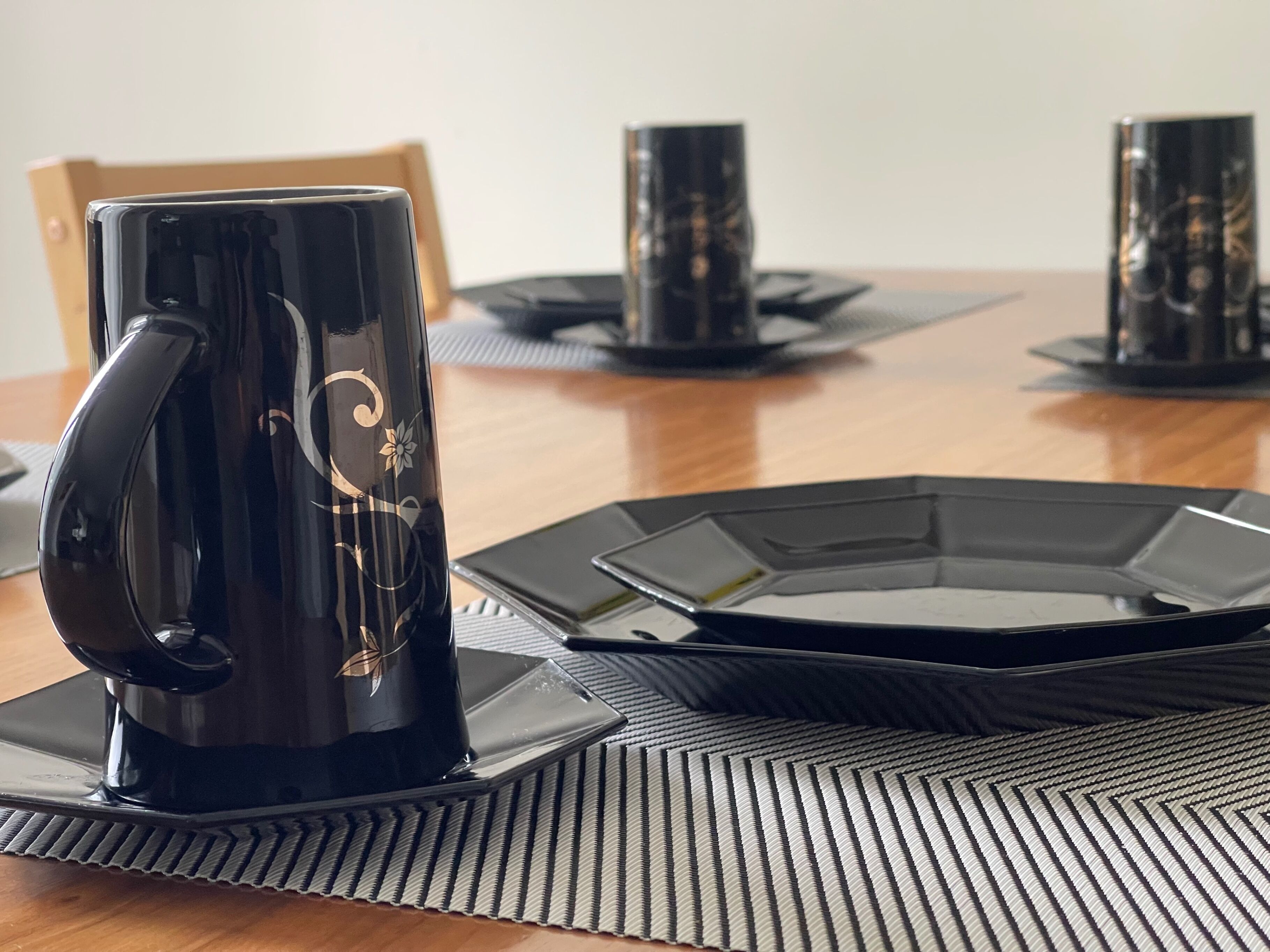 A dining table with a black coffee mug, a black plate, and a black napkin.
