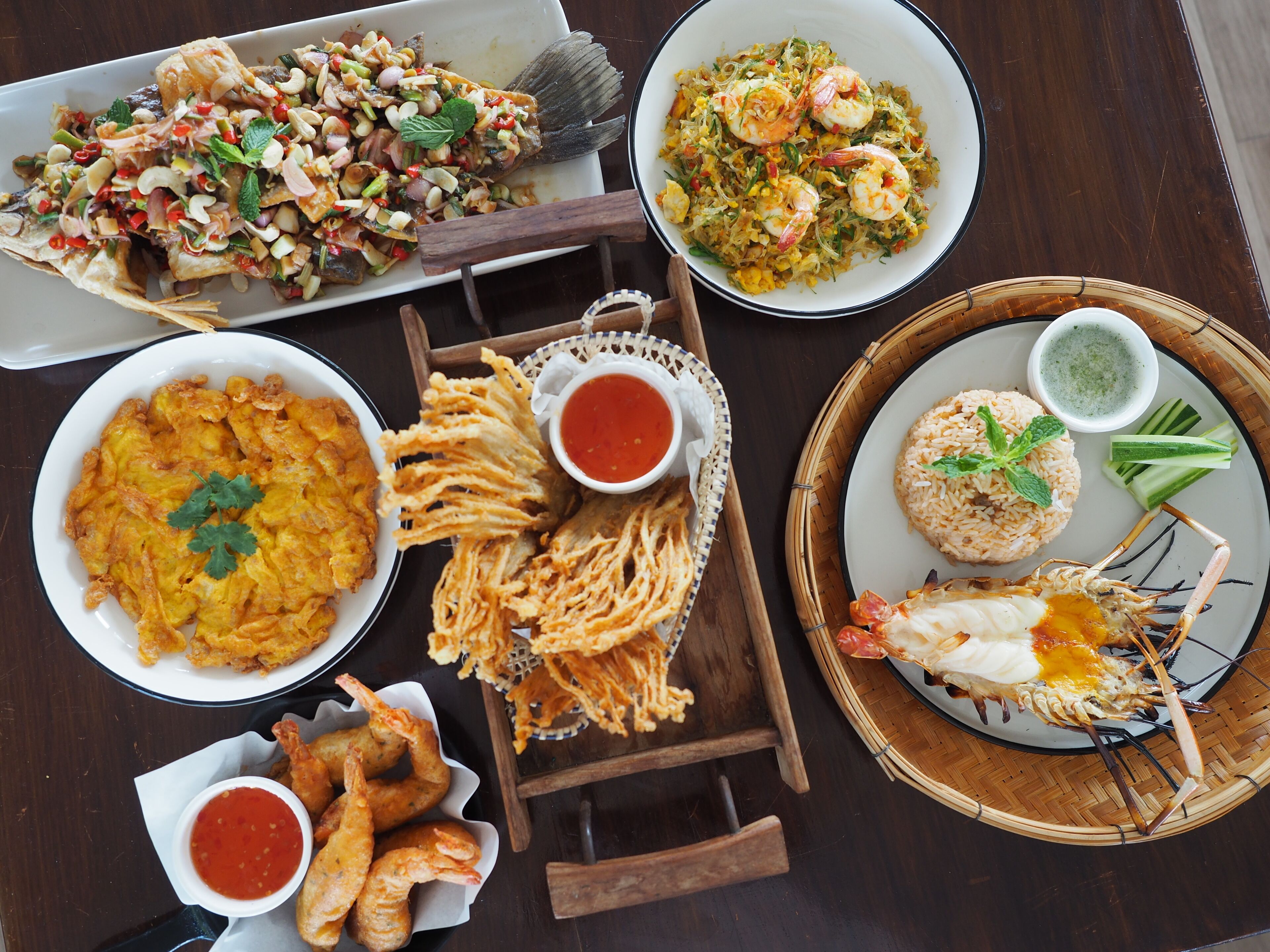 A variety of dishes including fried fish, rice, and shrimp served on a wooden table.
