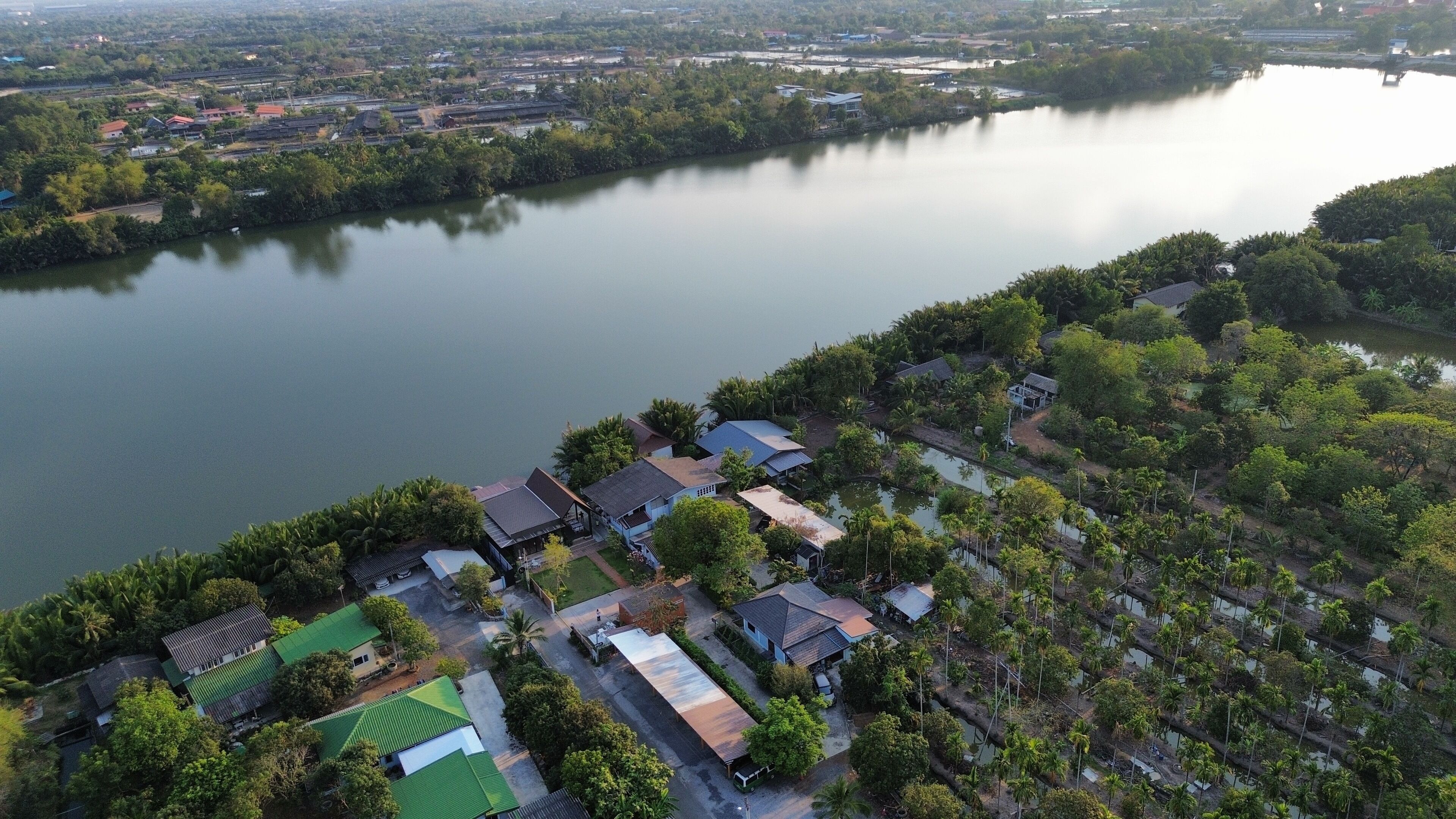 An aerial view of a residential area with houses along a river, surrounded by greenery.