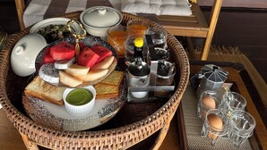 A breakfast setup with a wicker tray containing toast, fruit, and tea, a teapot, and a sugar dispenser. - House of moon phase (Chachoengsao)