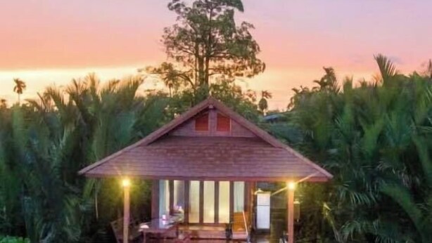 A wooden house with a porch, surrounded by water and palm trees, at sunset. - House of moon phase (Chachoengsao)