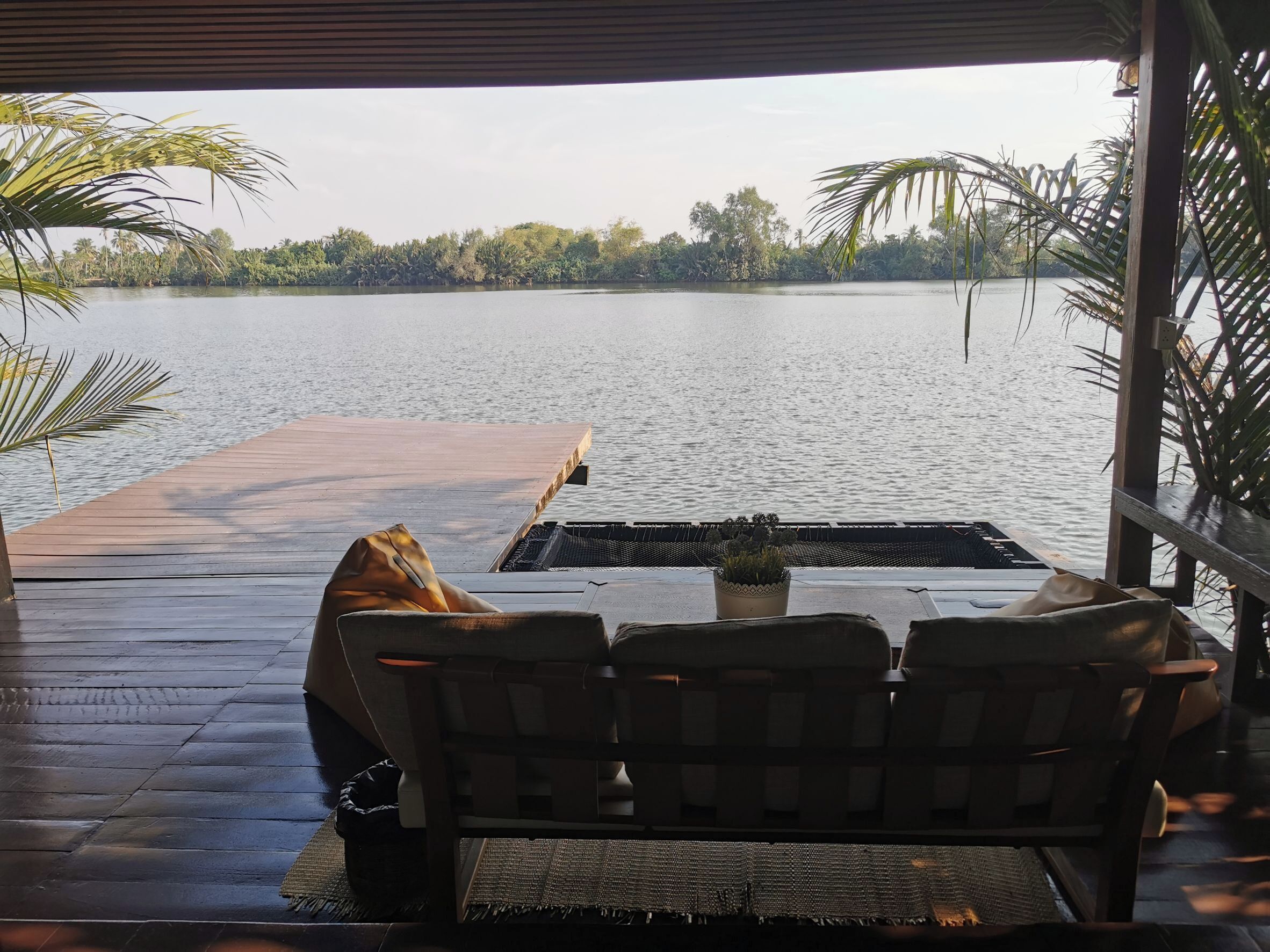 A wooden deck with a bench and a table, overlooking a calm lake with trees in the background.