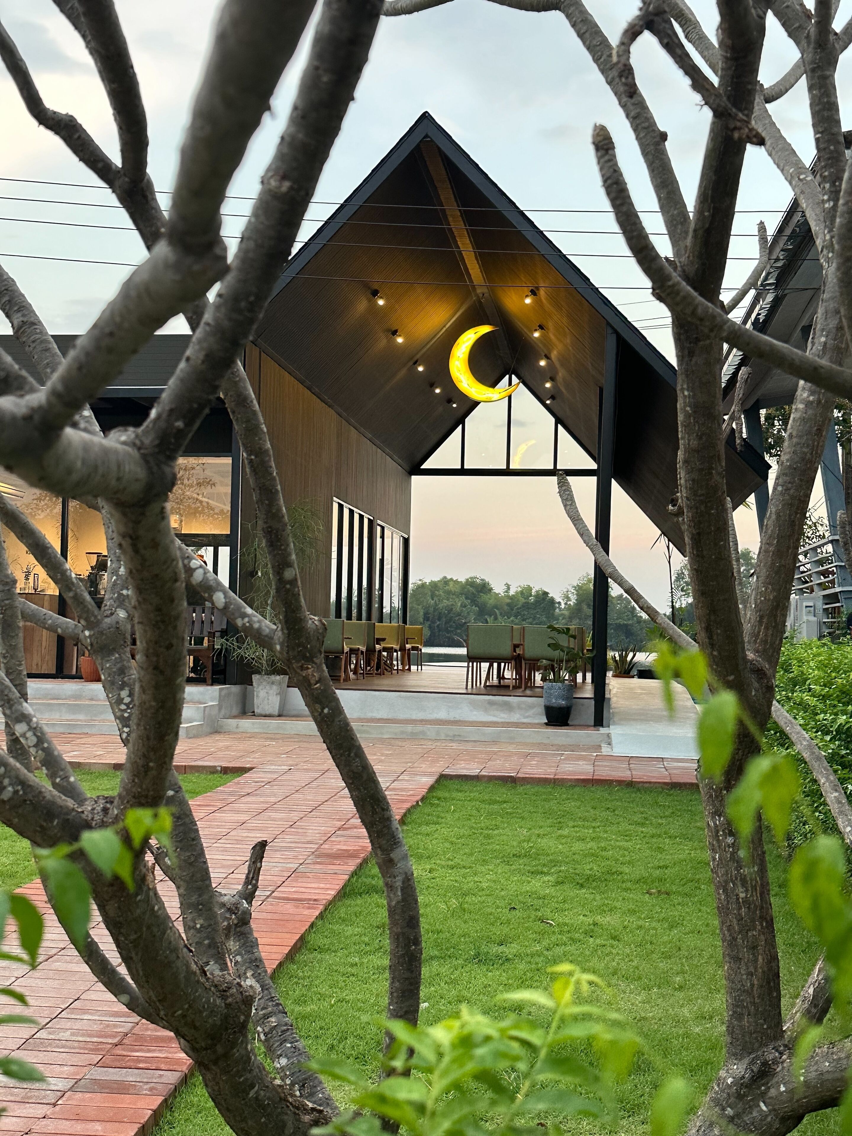 A modern building with a sloped roof, a crescent moon light fixture, and a patio area with chairs and tables.