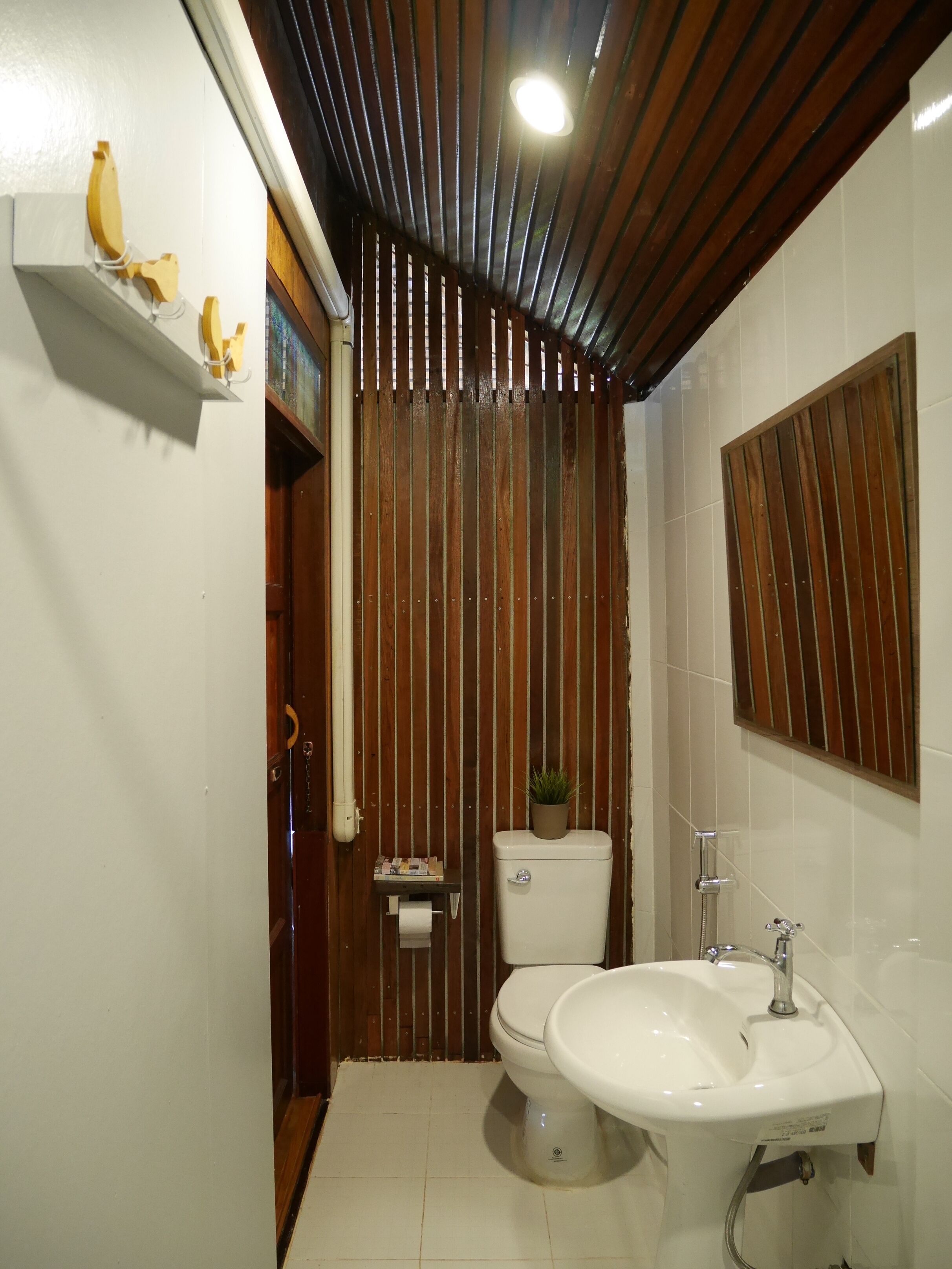 Un baño con pared de listones de madera, un inodoro, un lavamanos y un espejo.