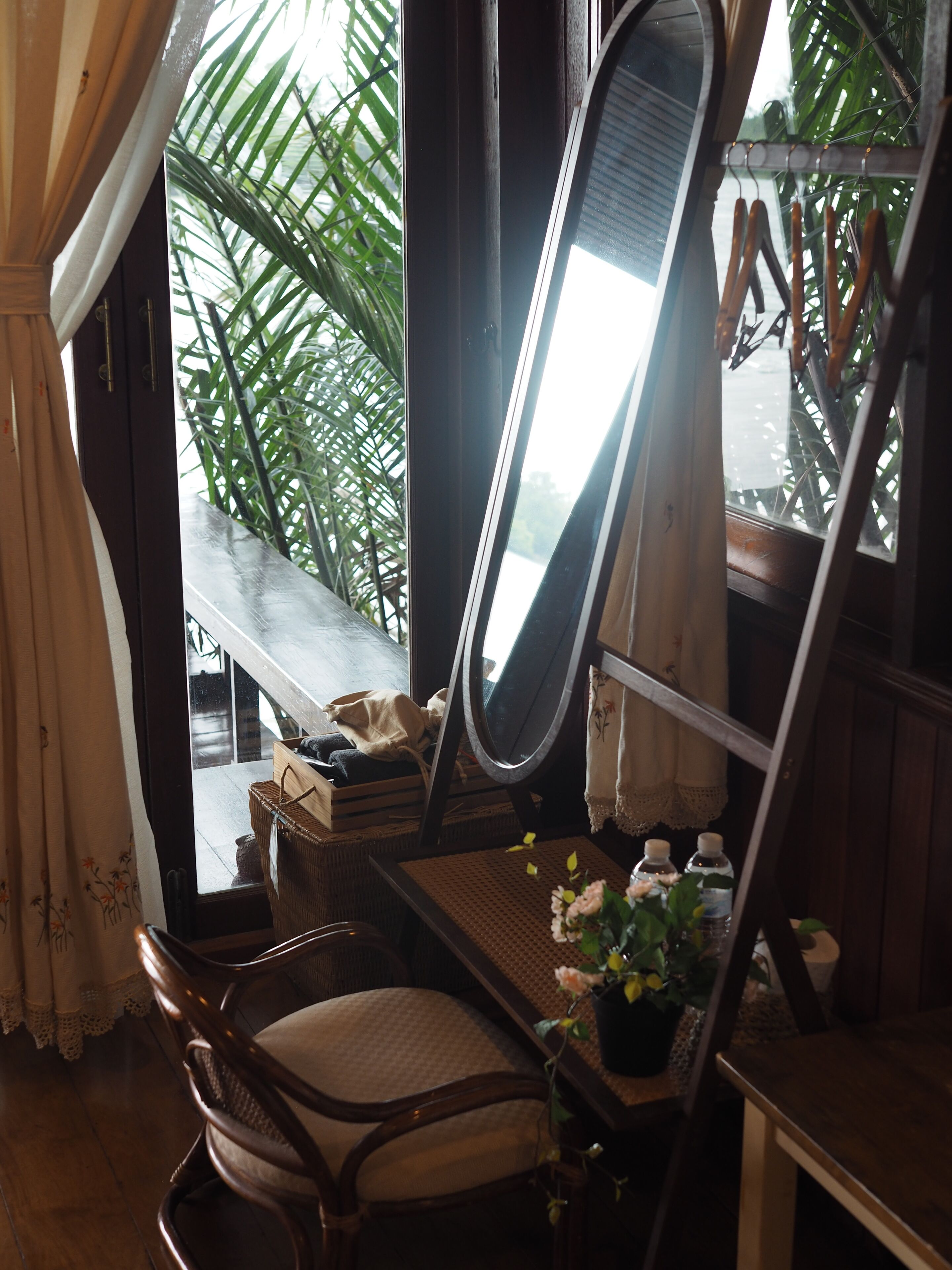A room with a wooden desk, a chair, a mirror, and a view of a balcony with plants.