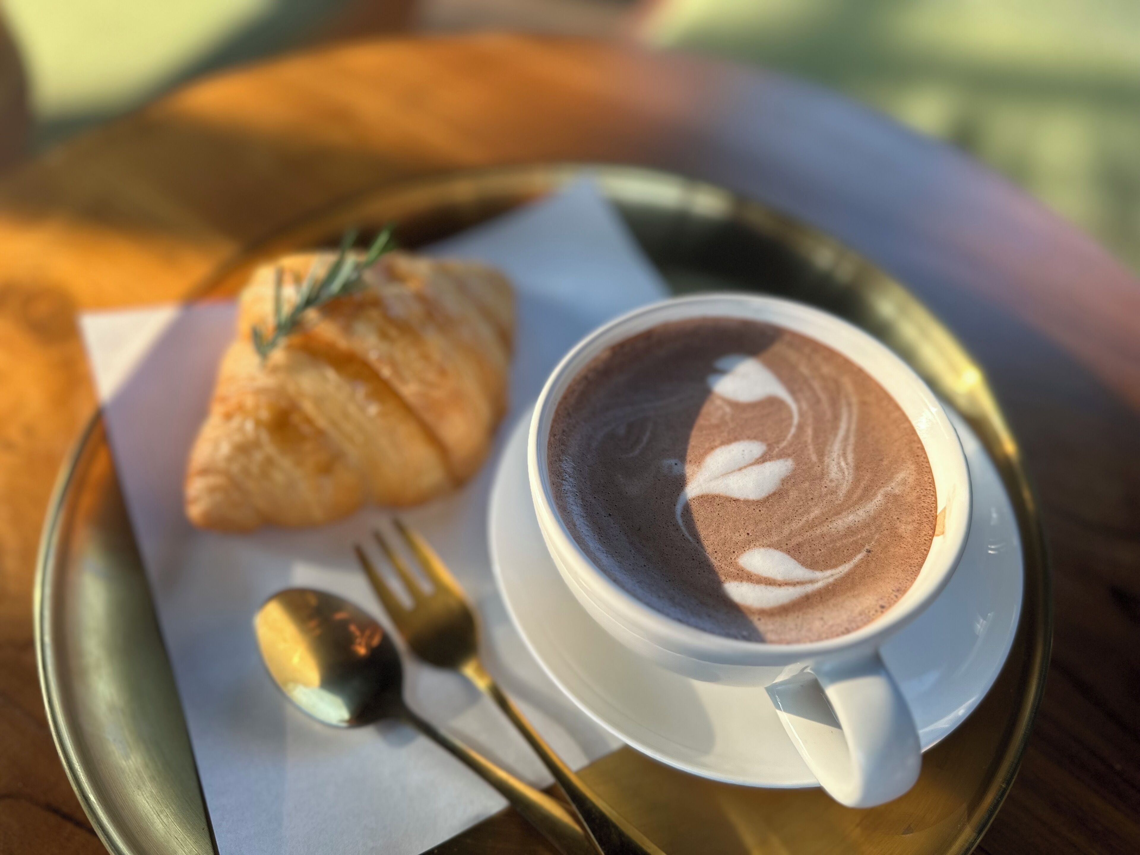 A tray with a croissant and a cup of coffee with latte art.