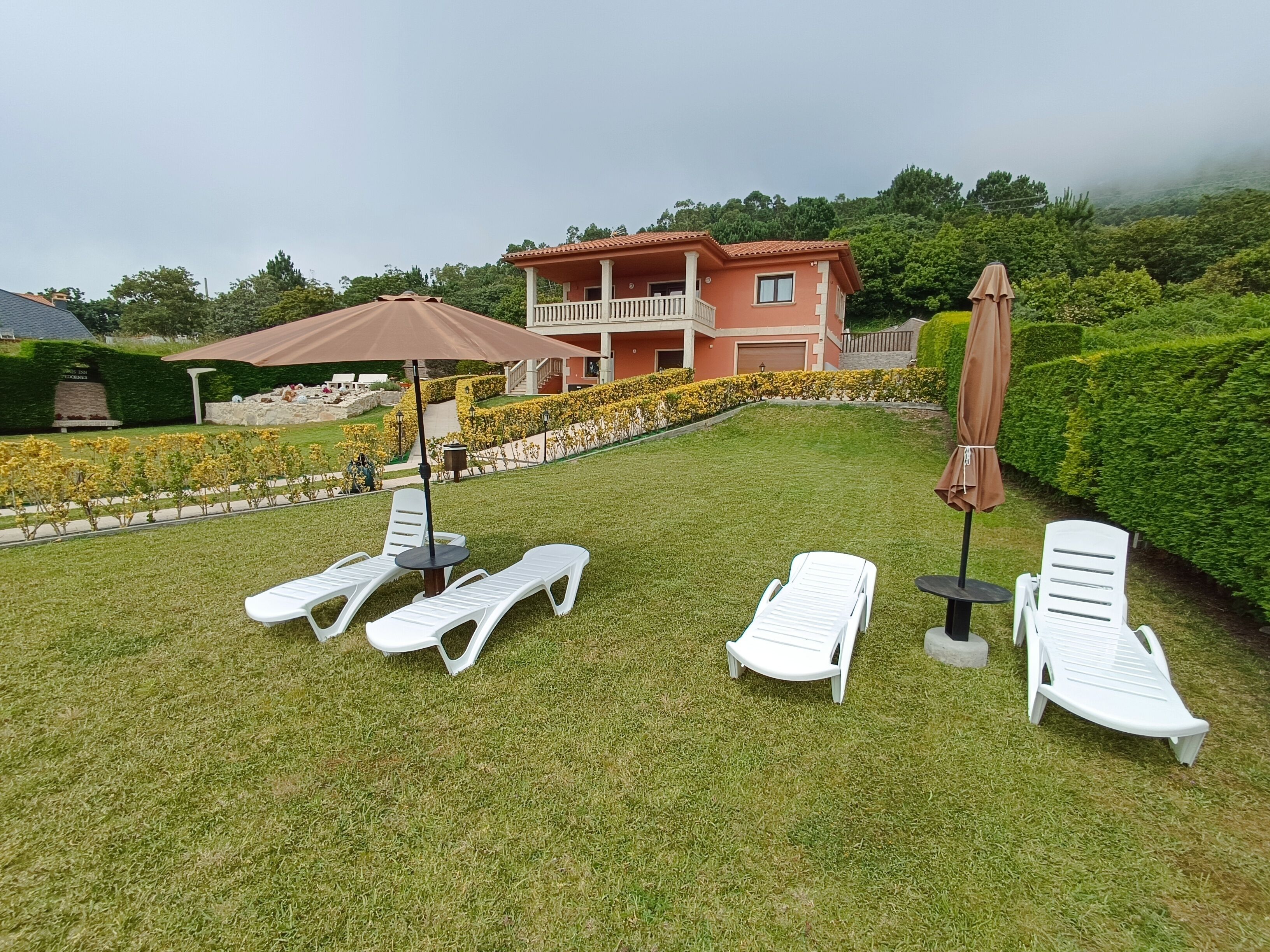 A well-maintained lawn with white lounge chairs and a table, surrounded by a neatly trimmed hedge and a building in the background.