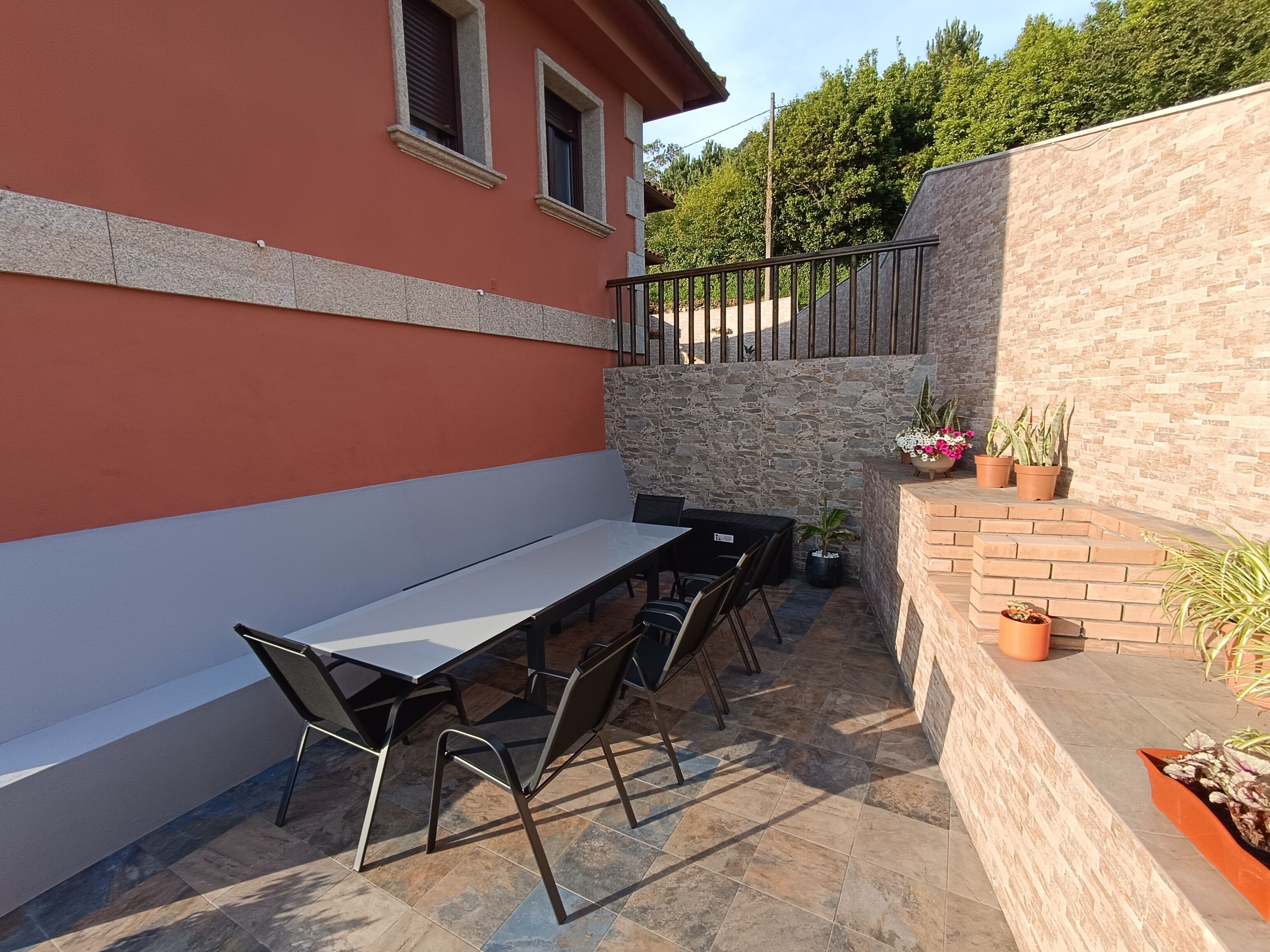 A patio area with a long table and chairs, a stone wall, and potted plants.