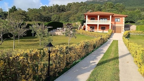 A two-story house with a red roof and white walls, surrounded by well-maintained gardens and a paved pathway leading to the entrance. - OASIS INN PEDORNES.A retreat between sea & mountains on Galicia’s Atlantic coast (Pedornes)