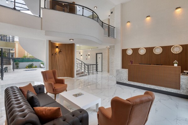 A spacious lobby with a curved staircase, a reception desk, and a seating area with leather sofas and armchairs. - Royal Dream's Hotel (Kemer)