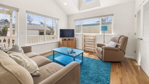A spacious living room with a high ceiling, large windows, a blue coffee table, a beige sofa, a recliner, and a TV. - Capitola Sea Winds one block to Capitola Beach (Capitola)