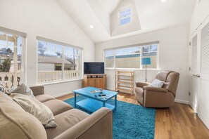 A spacious living room with a high ceiling, large windows, a blue coffee table, a beige sofa, a recliner, and a TV. - Capitola Sea Winds one block to Capitola Beach (Capitola)