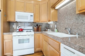 A kitchen with wooden cabinets, a white stove, a microwave, granite countertops, and a sink. - Capitola Sea Winds one block to Capitola Beach (Capitola)