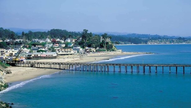 A coastal town with a pier extending into the sea, buildings along the shore, and a hilly backdrop. - Capitola Sea Winds one block to Capitola Beach (Capitola)
