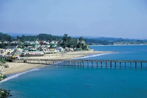 A coastal town with a pier extending into the sea, buildings along the shore, and a hilly backdrop. - Capitola Sea Winds one block to Capitola Beach (Capitola)