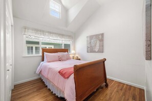 A bedroom with a wooden bed, white walls, a window with shutters, and a wall-mounted artwork. - Capitola Sea Winds one block to Capitola Beach (Capitola)